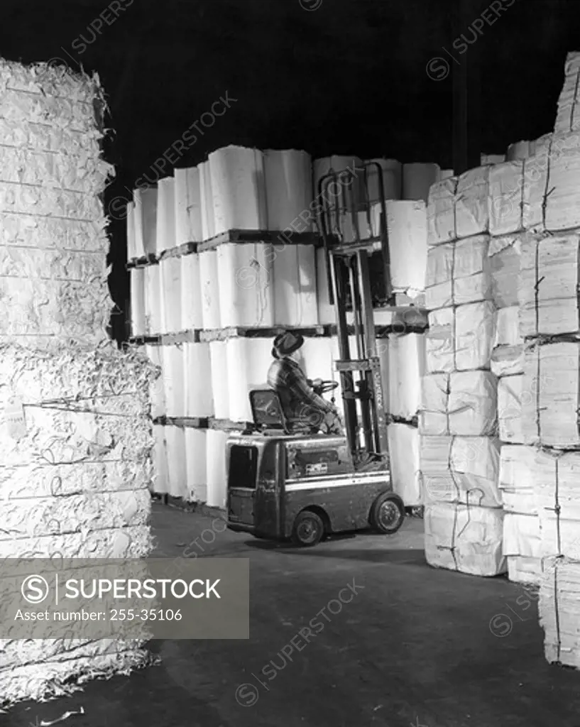 Rear view of a worker driving a forklift in a paper warehouse