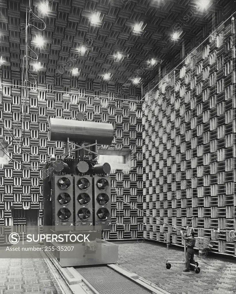 Vintage photograph. A large power transformer is being tested in the world's largest anechoic (without echoes) chamber, which is the main part of a new Sound Laboratory built for the General Electric Company Power Transformer Department. At right is a technician placing a microphone near the transformer