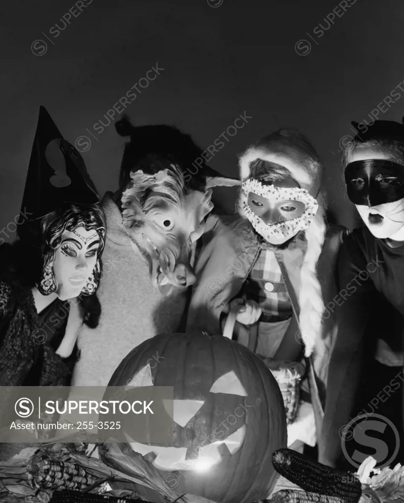 Four children wearing Halloween costumes looking at an illuminated jack o' lantern