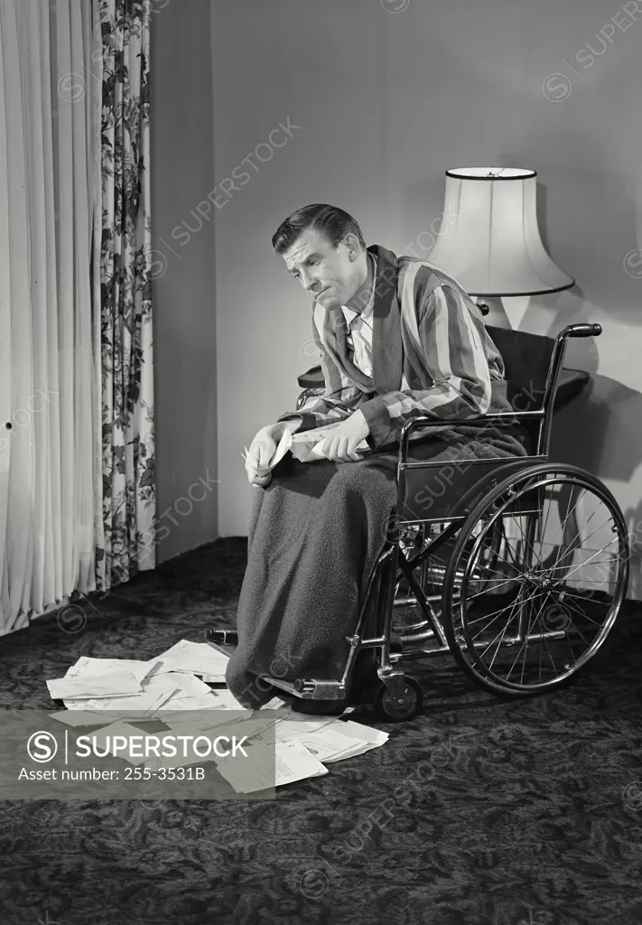 Vintage photograph. Man in wheelchair looking at insurance forms on floor