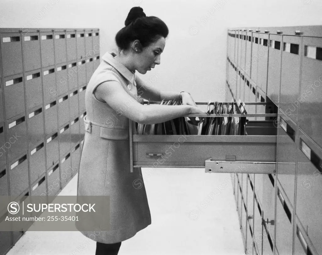 Side profile of a businesswoman searching for files in a filing cabinet