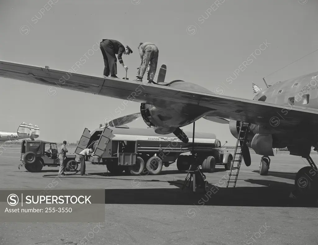 Vintage photograph. Low angle view of two people working on a wing of an airplane, New York International Airport, New York City, New York, USA