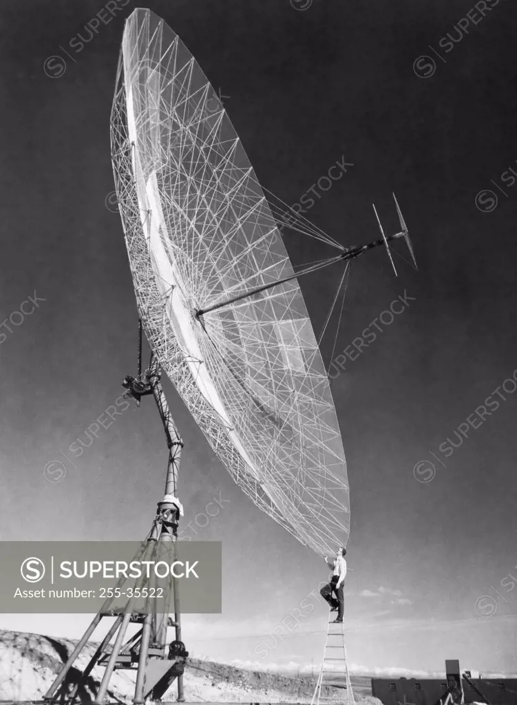 Side profile of an engineer standing on step ladder in front of a Parabolic antenna