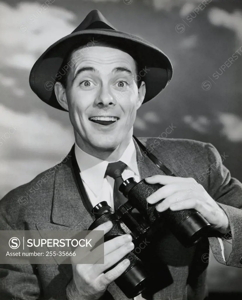 Vintage Photograph. Excited smiling man in suit holding up binoculars with strap around neck