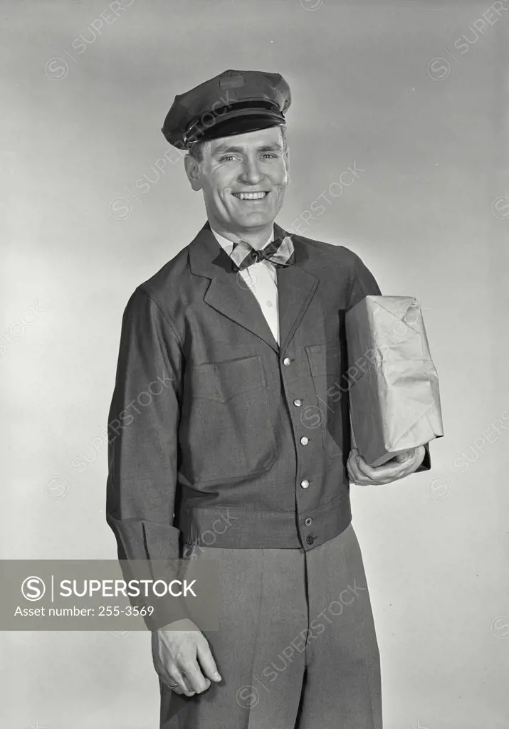 Vintage Photograph. Mailman in uniform holding package under arm smiling