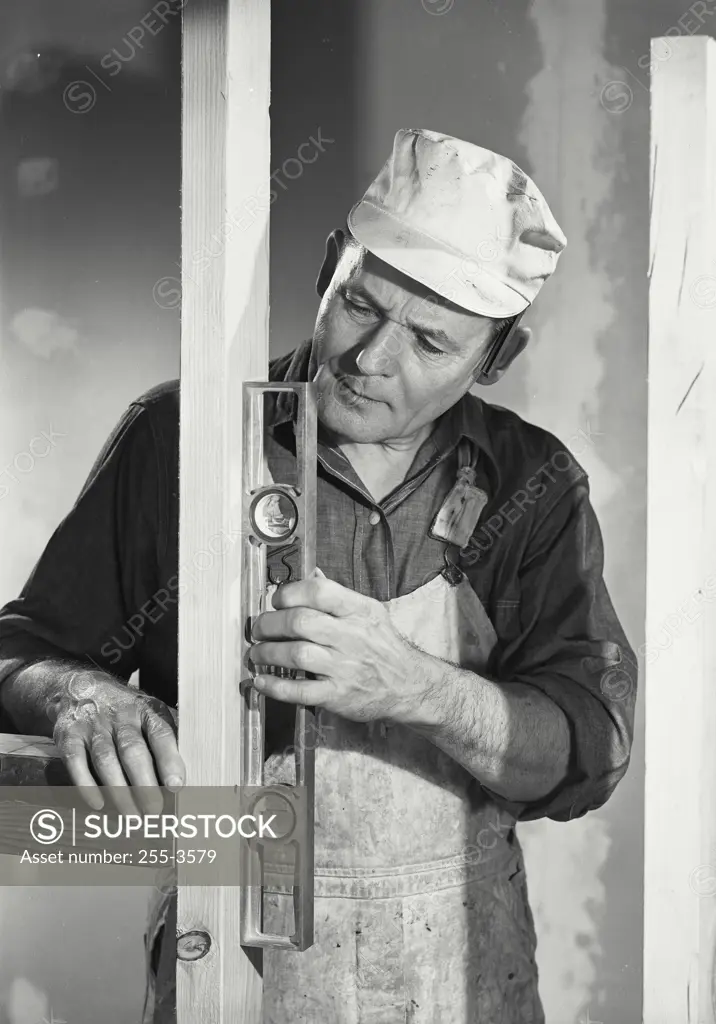 Vintage Photograph. Older carpenter using level tool to check wooden wall stud