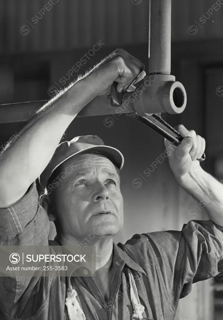 Vintage Photograph. Older working man looking up at wrench tightening overhead pipe