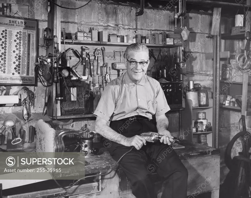Portrait of a senior man sitting in a workshop and holding a drill
