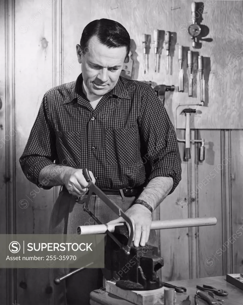 Mid adult man cutting a pipe with a saw in a workshop