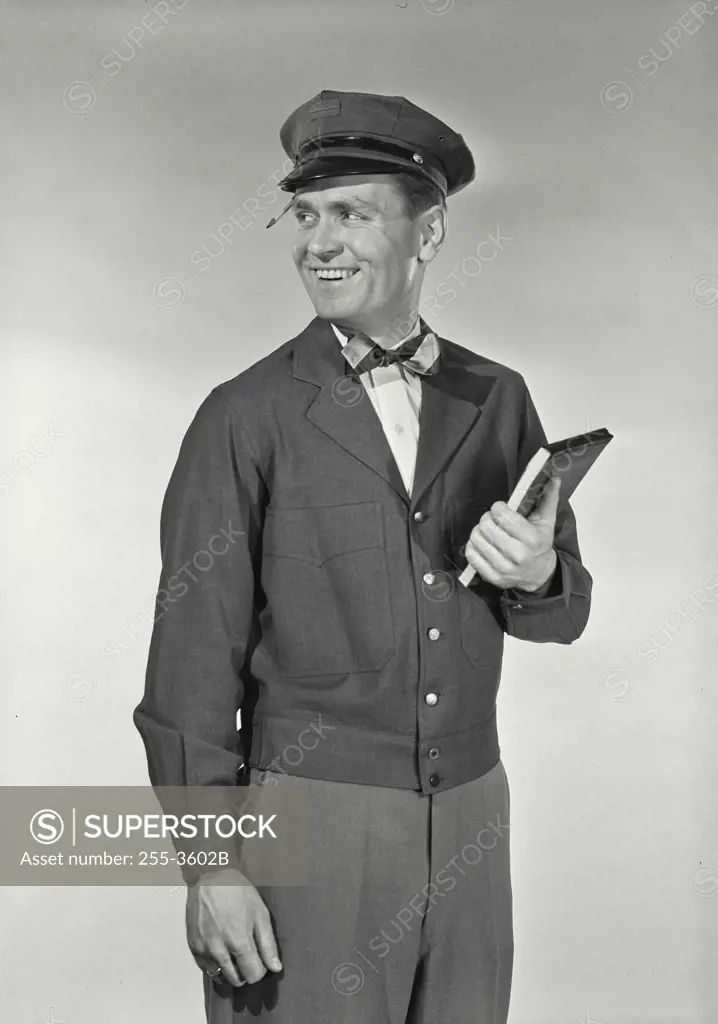 Vintage Photograph. Mailman in uniform with pencil stuck in hat brim holding up notepad smiling