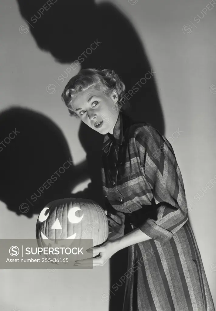 Vintage photograph. Side profile of a young woman holding an illuminated jack o' lantern