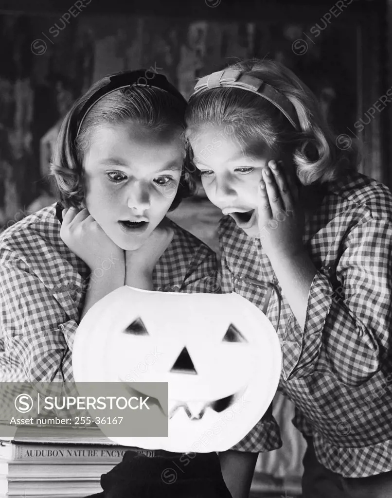 Close-up of two girls looking at an illuminated jack o' lantern