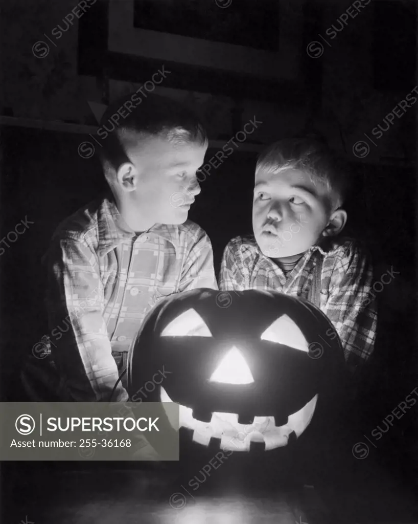 Two boys sitting behind an illuminated jack o' lantern
