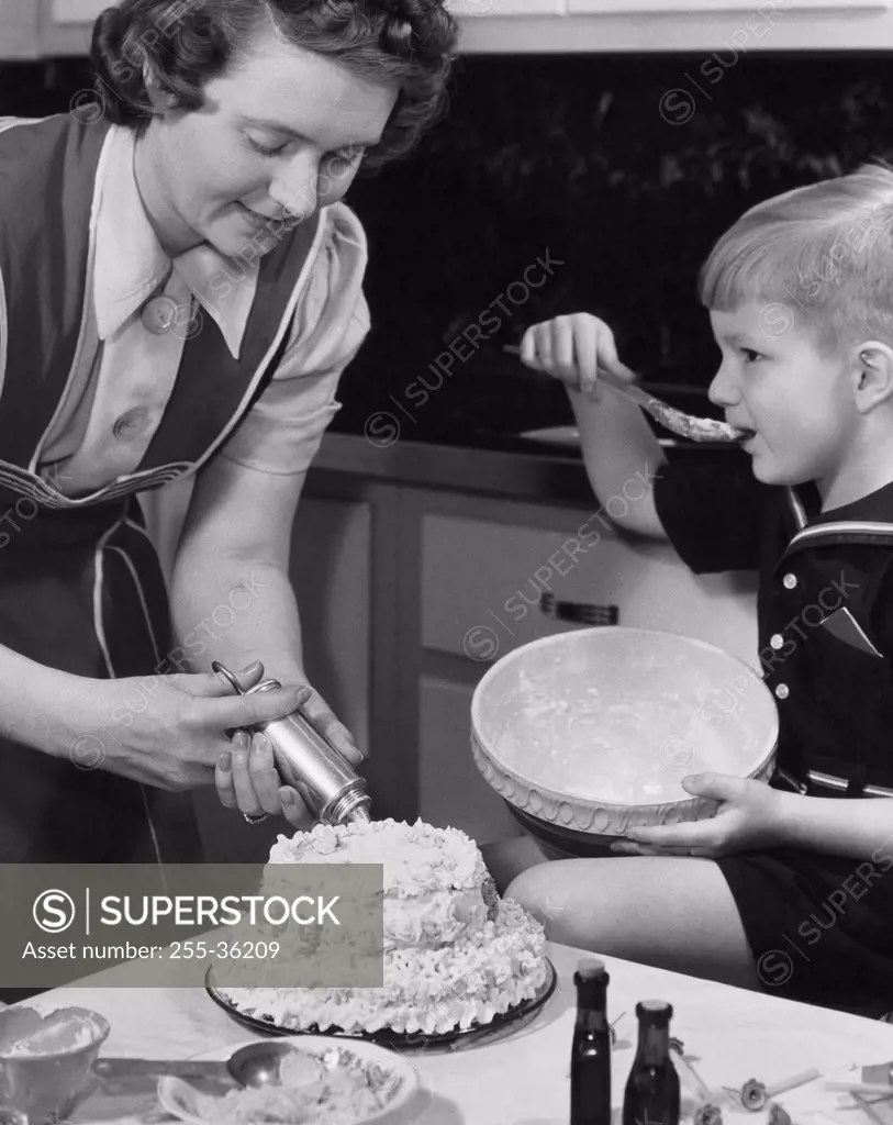 Mid adult woman preparing a cake with her son sitting beside her