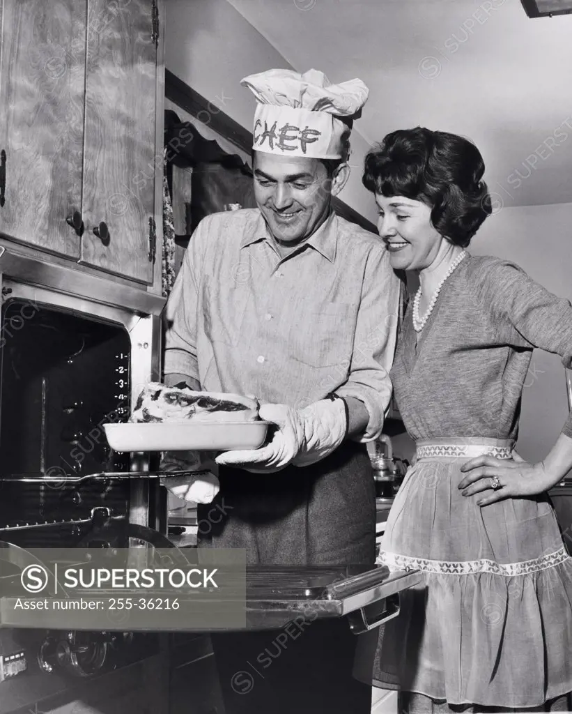 Mid adult man taking food out of an oven with a mid adult woman standing beside him