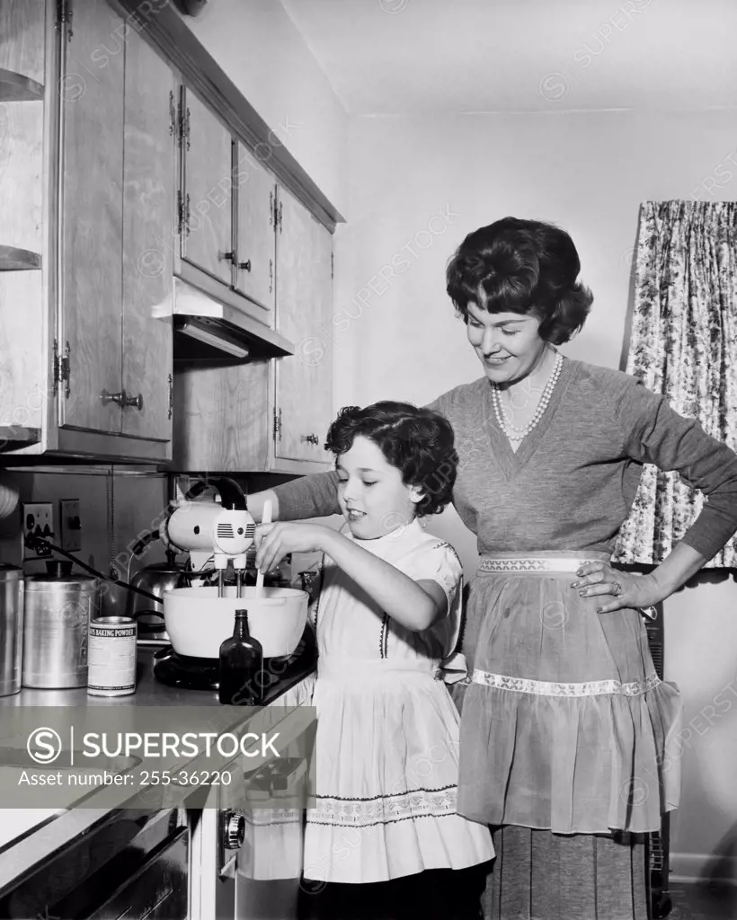 Side profile of a girl preparing food in the kitchen with her mother standing beside her