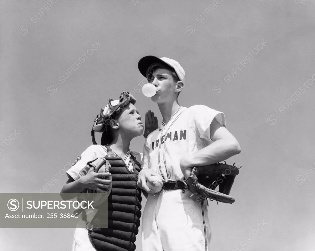 Low angle view of a youth league pitcher blowing a bubble of a bubble gum with catcher standing beside him