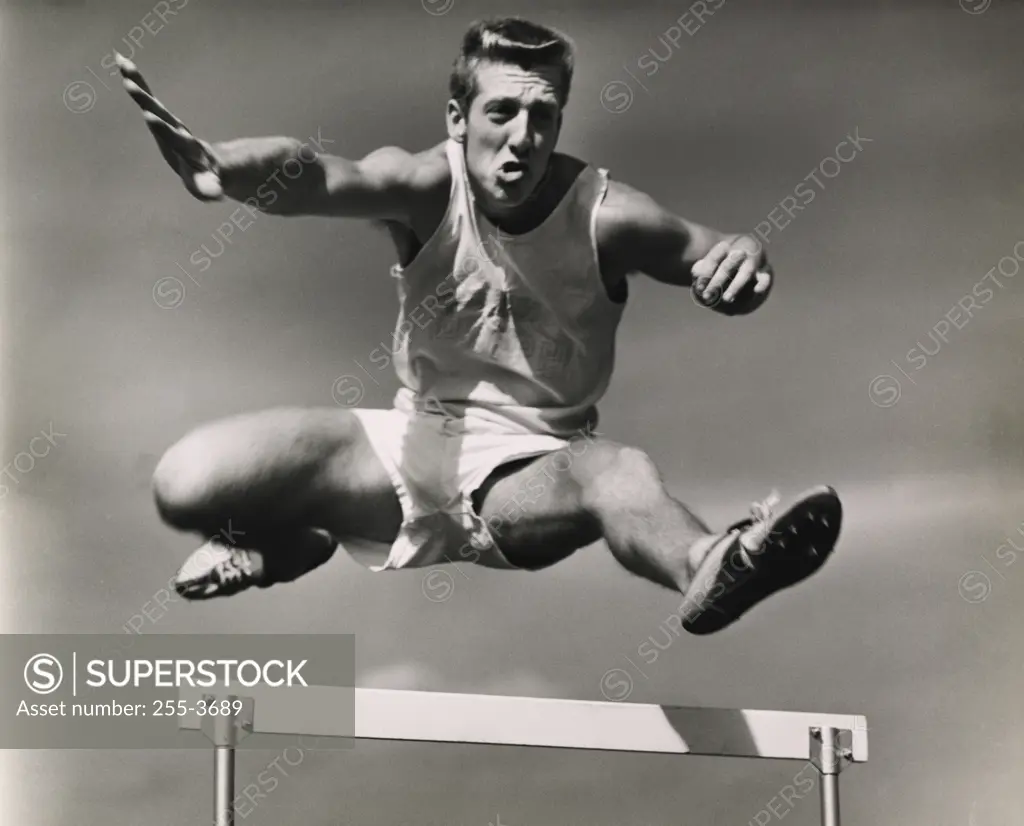 Low angle view of a male athlete jumping over a hurdle