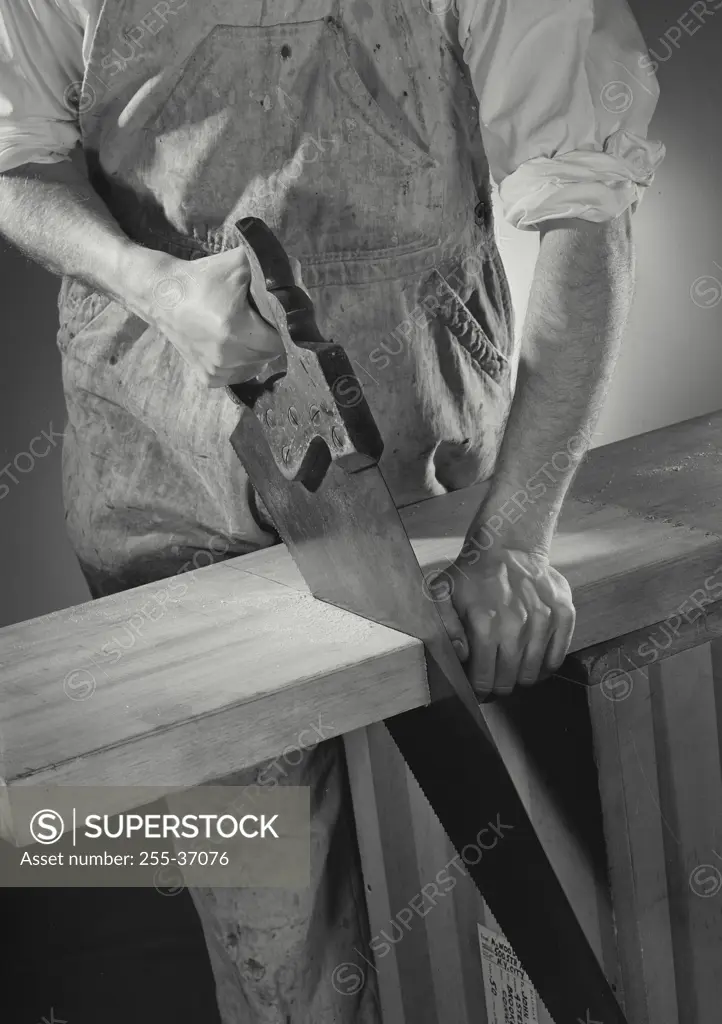 Vintage Photograph. Man cutting through thick wooden board with hand saw