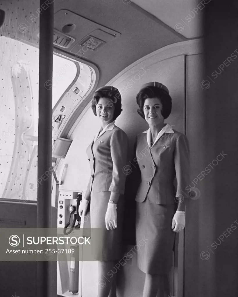 Two flight attendants standing on an airplane and smiling