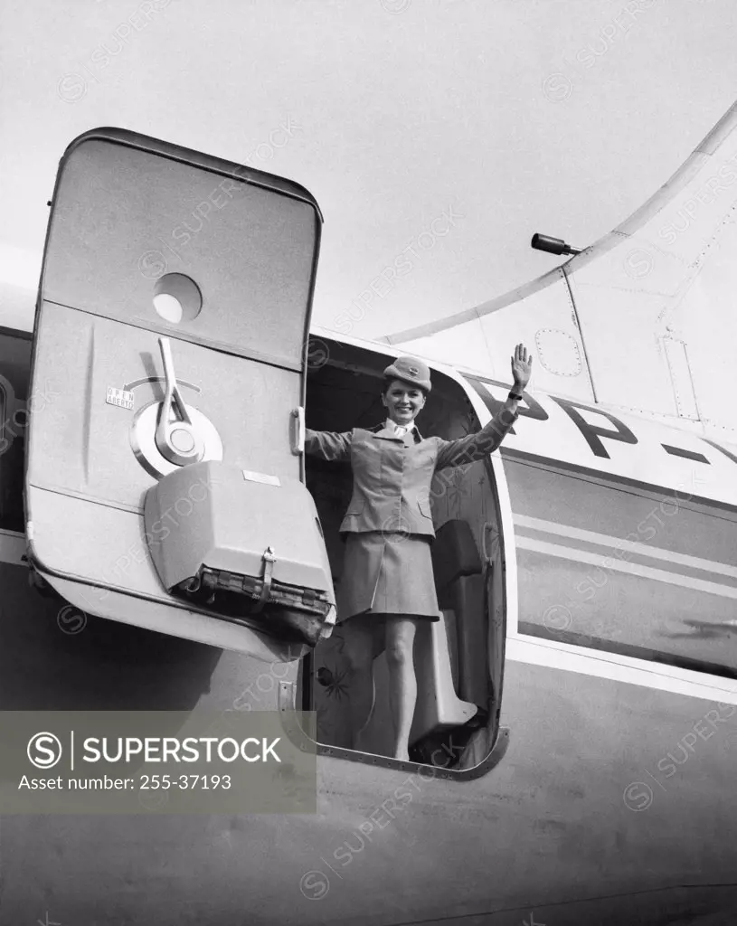 Low angle view of a female flight attendant standing at the open door of an airplane and waving