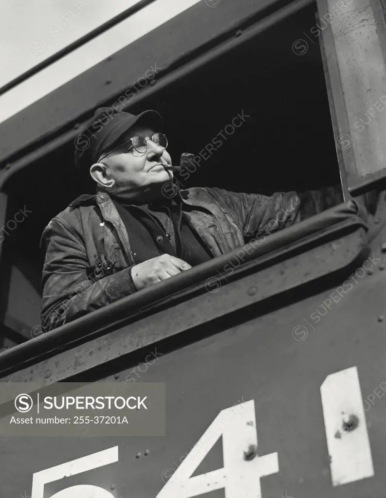 Vintage photograph. Engineer looking out of cab of a diesel locomotive with pipe in mouth