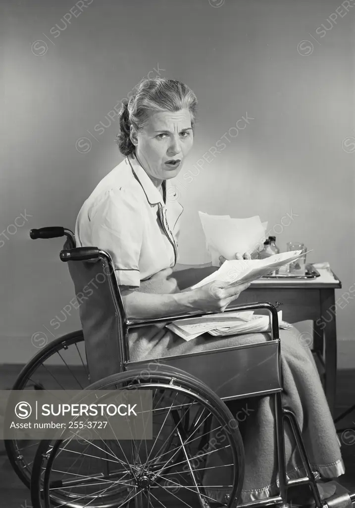 Vintage photograph. Woman in wheelchair reading insurance forms looking upset
