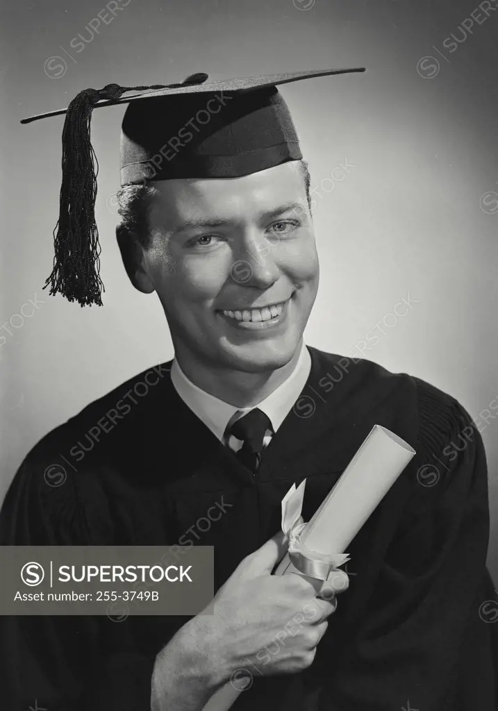 Vintage photograph. Portrait of man in cap and gown holding rolled diploma and smiling