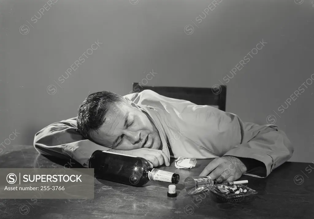 Vintage Photograph. Man passed out drunk on table with empty liquor bottle and ashtray filled with cigarettes, Frame 1