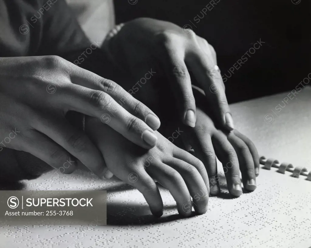 Close-up of an adult helping a blind child read Braille script