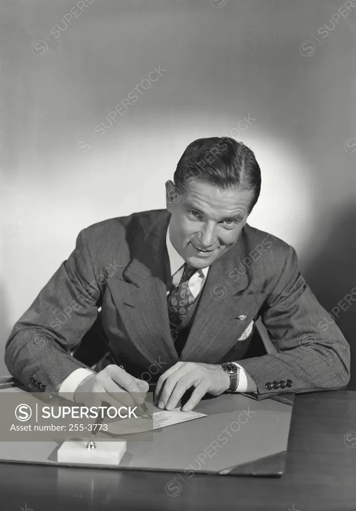 Man in suit sitting at desk signing check