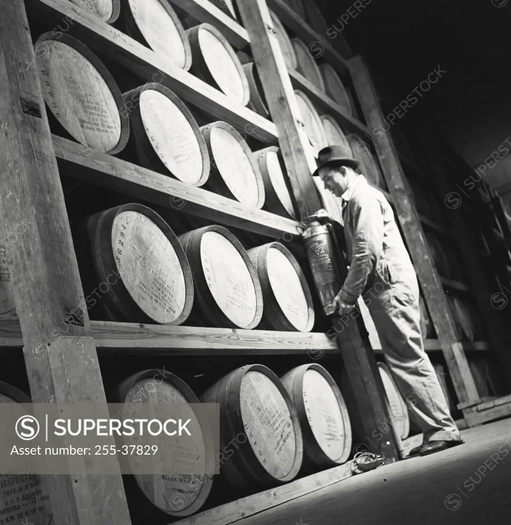 Vintage photograph. Man standing next to whiskey barrels in storage at Seagram's Whiskey facility