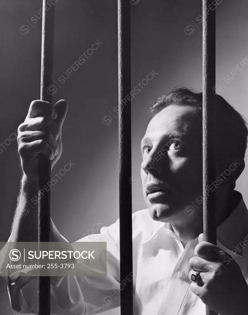 Close-up of a male prisoner holding prison bars