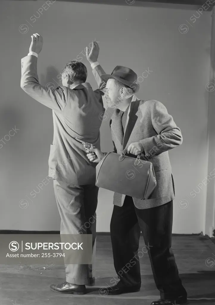 Vintage Photograph. Man with gun holding bag robbing man turned away with hands raised, gun pointing in his back, Frame 1