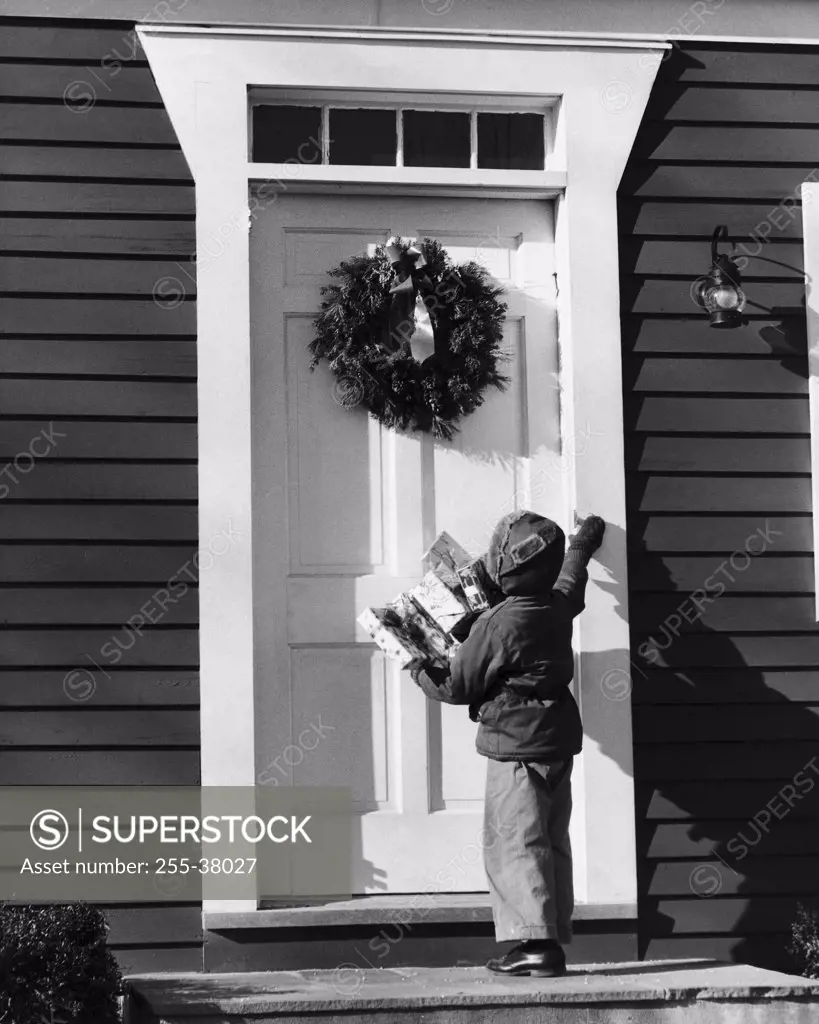 Rear view of a boy holding Christmas presents and standing in front of a closed door