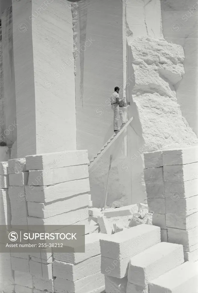 Vintage Photograph. Worker quarrying blocks of limestone on ladder for home building construction