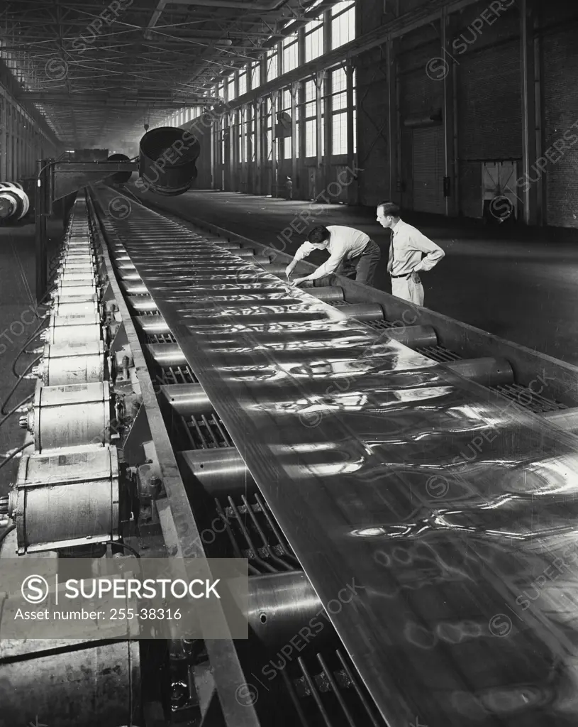 Vintage Photograph. Men inspecting strip of aluminum sheet as long as two city blocks after being pressed through large rolling mills. Aluminum Company of America