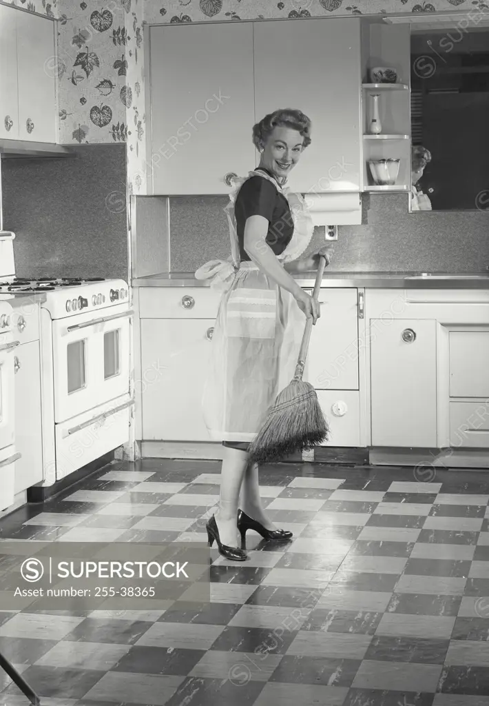 Vintage Photograph. Woman wearing apron sweeping in kitchen.
