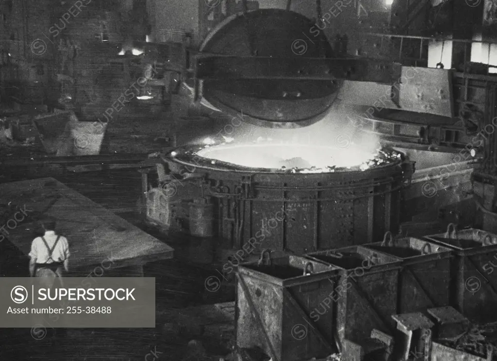 Vintage photograph. The crucible of an electric furnace is reloaded with scrap steel at a British steel factory. It takes about four hours to melt twenty or thirty tons of steel.