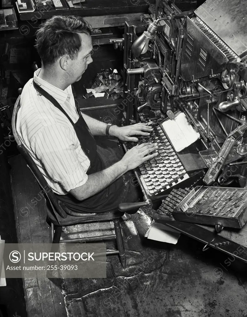 Vintage photograph. High angle view of a male worker operating a linotype machine