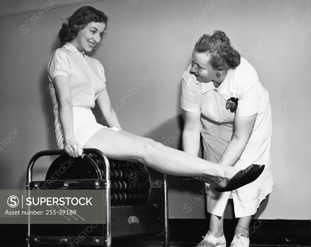 Young woman exercising on an exercising machine with the help of a female instructor