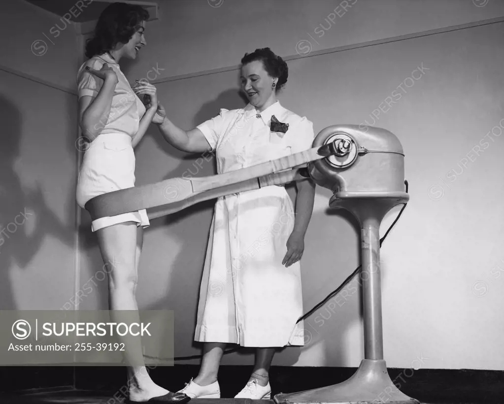 Side profile of a young woman leaning against the belt of a slimming machine with her instructor checking her pulse