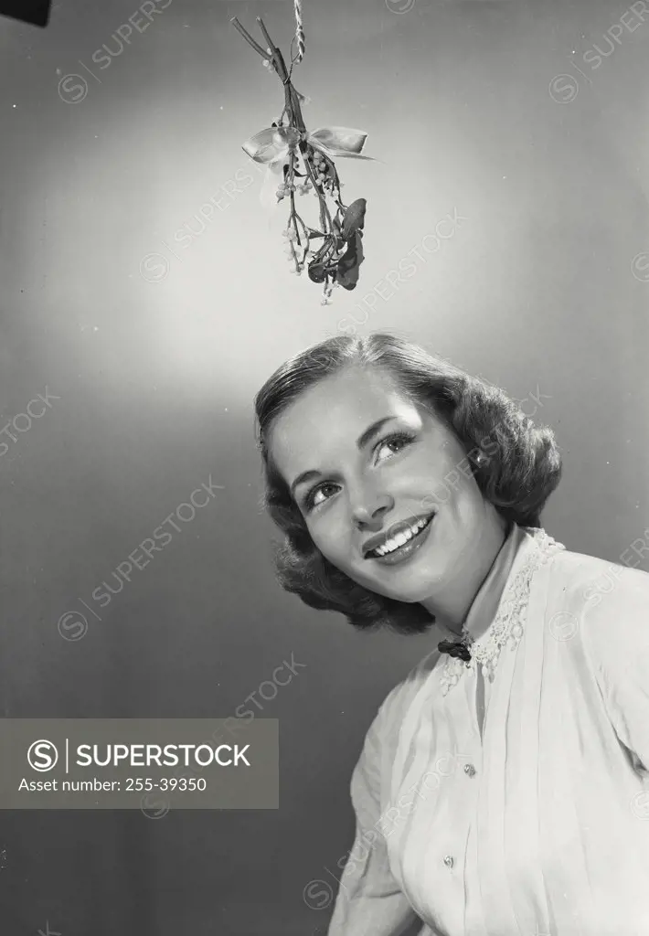 Portrait of young woman in white blouse looking up at misletoe hanging above her head