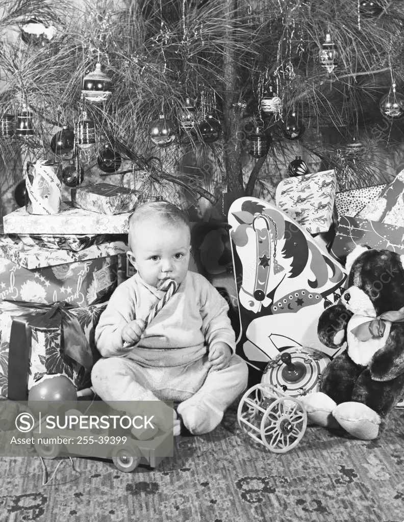 Boy sitting near Christmas presents and eating a candy cane