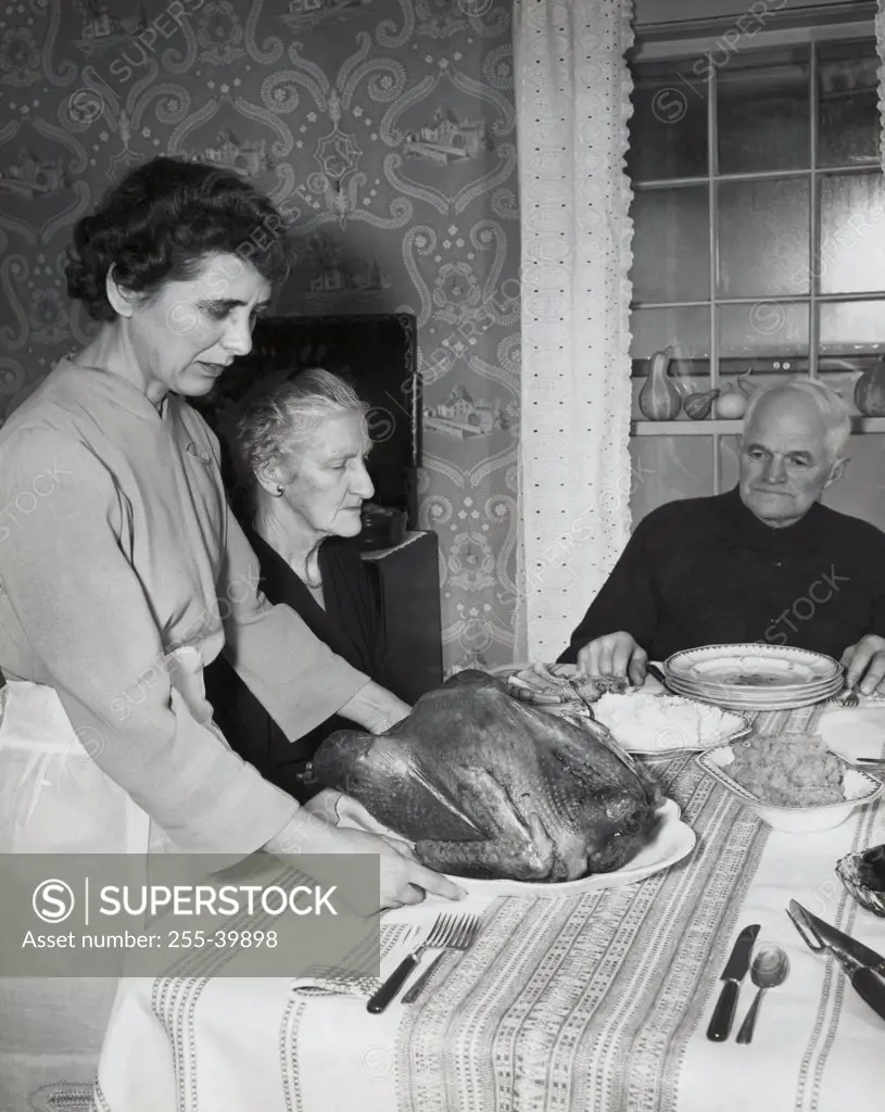 Side profile of a mature woman serving a roasted turkey to her parents on Thanksgiving Day