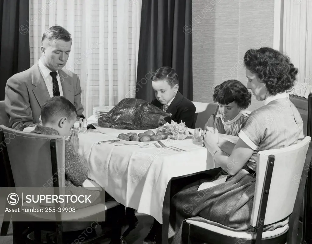 Mature couple with their children praying at a dining table on Thanksgiving Day