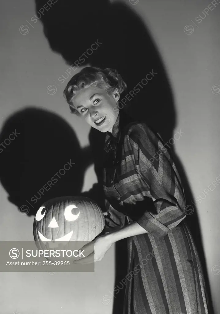 Vintage photograph. Side profile of a young woman holding a carved Halloween pumpkin