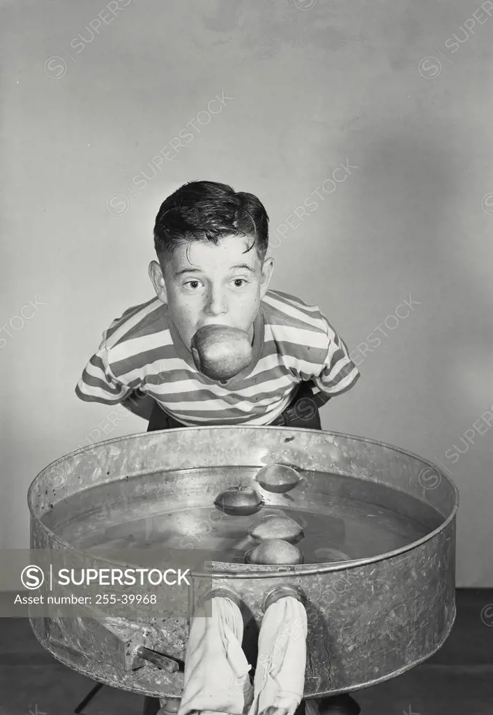 Vintage photograph. Boy with eyes wide open bobbing for apples behind water tank