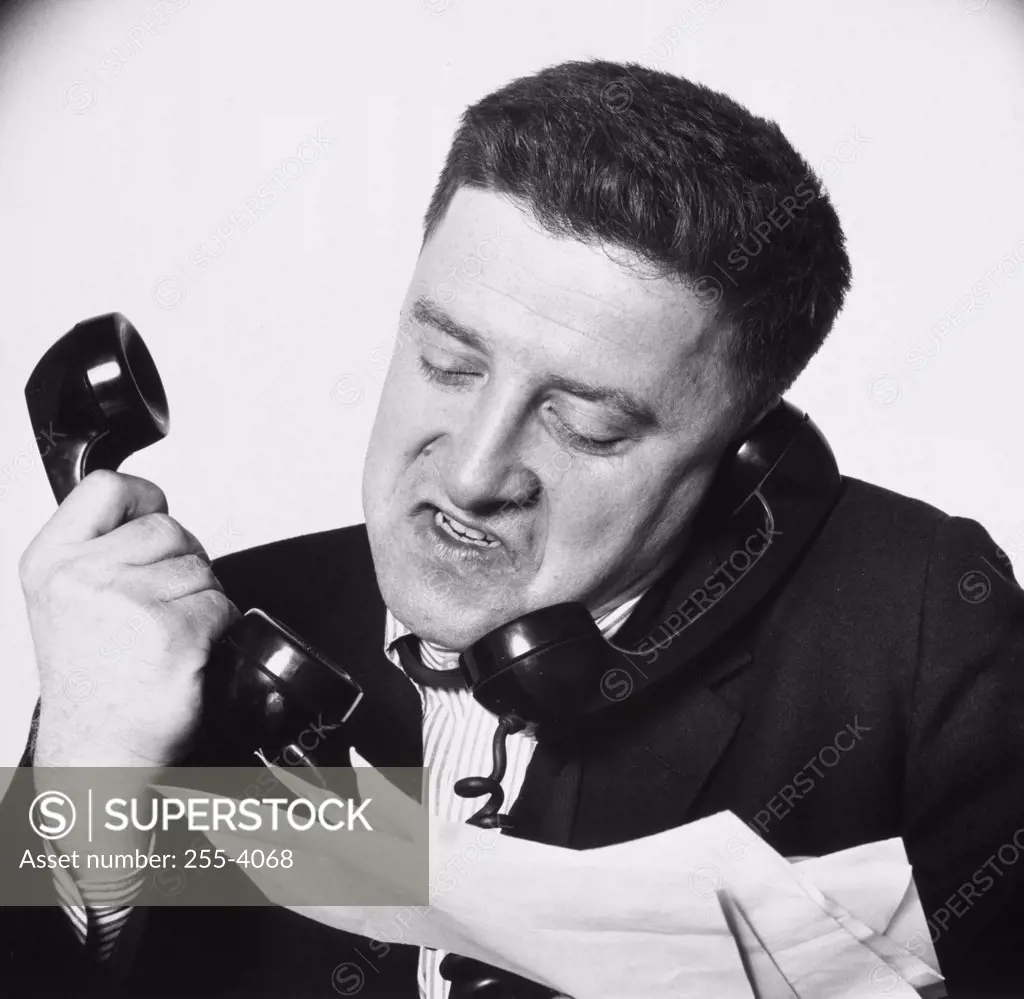 Close-up of a businessman using two telephones looking frustrated