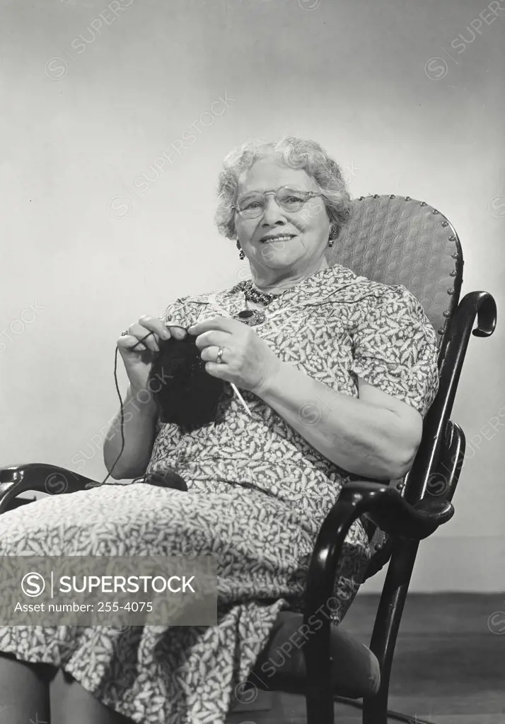 Smiling elderly woman sitting in rocking chair knitting